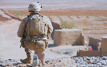 Soldier in the field crouching down looking out over a desert town